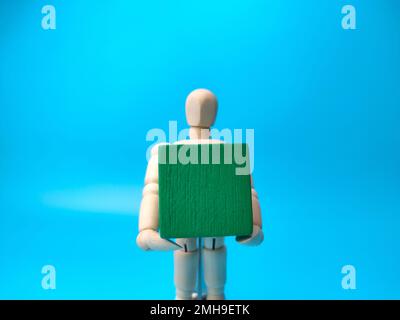 Wooden mannequin holding blank wooden block on blue background. Copy and text space concept. Stock Photo
