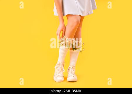 Legs of beautiful young woman with flowers in socks on yellow background Stock Photo