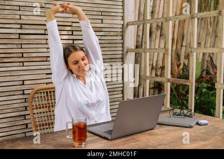 Young positive business woman sit indoors in co working using laptop computer. Stock Photo