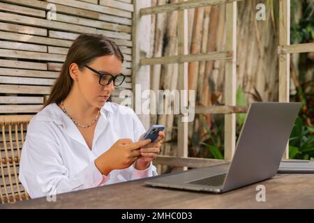 Attractive young woman using smartphone and laptop computer in summer cafe Stock Photo
