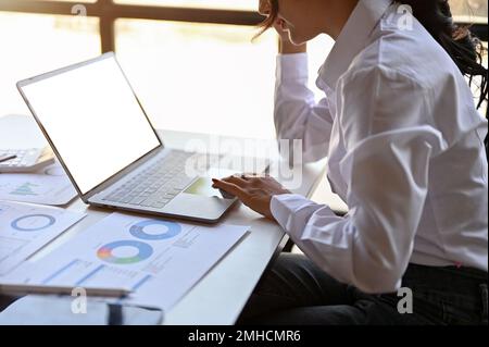 side view of an Asian female financial analyst or accountant working on business financial data report at her desk, using laptop computer. cropped sho Stock Photo