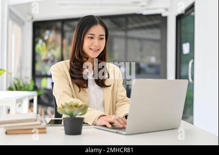 Attractive millennial Asian businesswoman working in the office, using laptop computer, making her presentation slides on laptop. Stock Photo