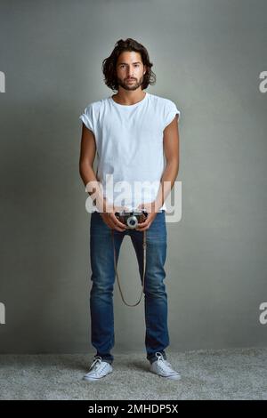 Hes got an eye for photography. Studio portrait of a handsome young man holding a vintage camera against a grey background. Stock Photo