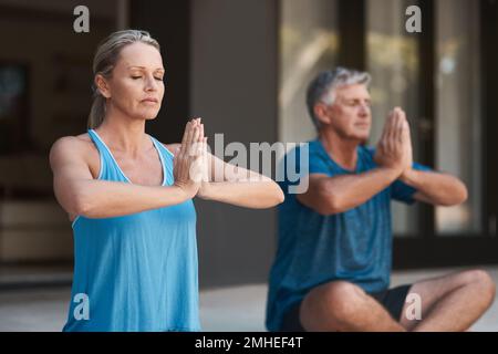 Focus the mind and youll find peace. a mature couple peacefully engaging in a yoga pose with legs crossed and hands put together. Stock Photo