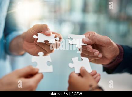 Putting pieces of their plan together. a group of unrecognizable businesspeople putting puzzle pieces together in the office. Stock Photo