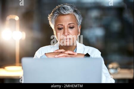 Senior woman, doctor and laptop at night thinking for healthcare solution, idea or strategy at hospital. Elderly female medical expert working late on Stock Photo