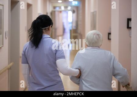 PRODUCTION - 24 January 2023, Hesse, Frankfurt/Main: Irina Ushakova, a nurse from Ukraine, walks down the corridor with a resident at the GDA Wohnstift Frankfurt am Zoo. Thousands of Ukrainians have found work in Hesse after fleeing the war in their homeland. One of them is Irina Ushakova, a trained nurse. (to dpa-KORR New professional start after flight: 'Now a new chapter begins') Photo: Sebastian Gollnow/dpa Stock Photo