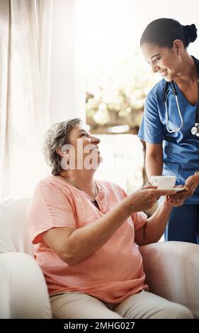 Thanks for making me such a lovely cuppa. an attractive young female caregiver offering a cup of tea to a senior patient in a nursing home. Stock Photo