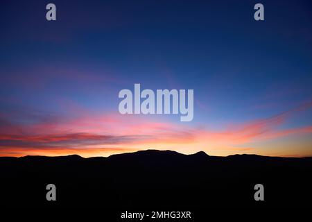 Landscape long exposure of majestic clouds in the sky sunset or sunrise over mountains. Beautiful colourful cloudscape scenery with silhouette of Stock Photo