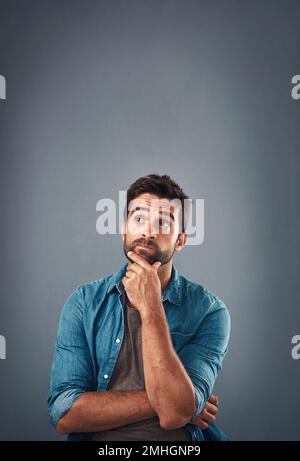 Having an um moment. Studio shot of a handsome young man looking thoughtful against a grey background. Stock Photo