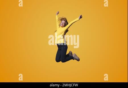 Full length body size photo of a woman jumping high gesturing like winner isolated on yellow color background.