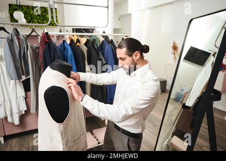 Experienced tailor is trying on vest on mannequin Stock Photo