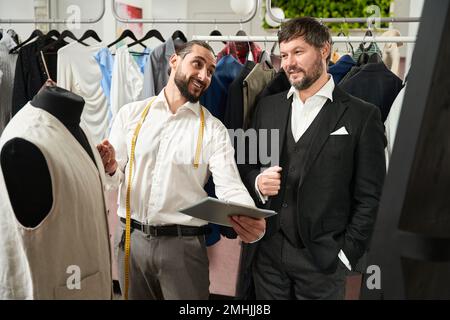 Cheerful tailor communicating with client in his atelier Stock Photo