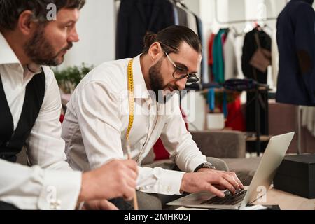 Two modern clothiers using laptop in atelier Stock Photo