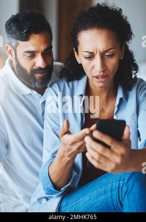Where did all our money go. a dismayed couple receiving bad news via a smartphone at home. Stock Photo