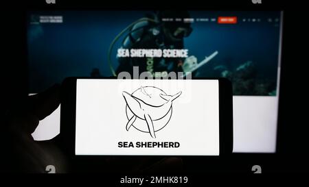 Person holding cellphone with logo of Sea Shepherd Conservation Society (SSCS) on screen in front of webpage. Focus on phone display. Stock Photo