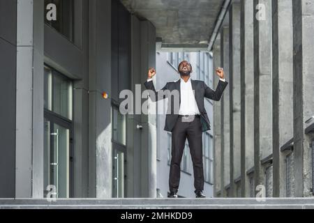 African american boss celebrating victory and successful achievement, businessman dancing on stairs of modern office building. Stock Photo