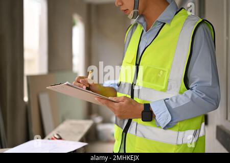 Engineer man in reflective jackets writing on clipboard, inspecting building construction site Stock Photo