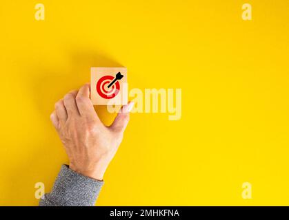 Hand holding a wooden cube with a red target and arrow, representing goals and success. Stock Photo