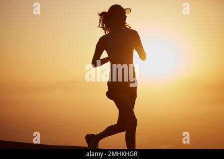 This princess wears running shoes. a silhouetted young woman out for a run at sunrise. Stock Photo