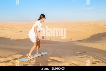 Young women sand surfing at the sand dunes of Dubai United Arab Emirates, sand desert on a sunny day in Dubai. Stock Photo