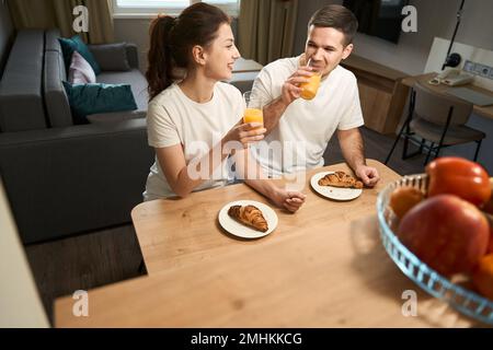Joyful young couple is having breakfast at a wooden table Stock Photo