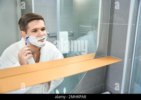 Close up of young man shaves in front of a mirror Stock Photo