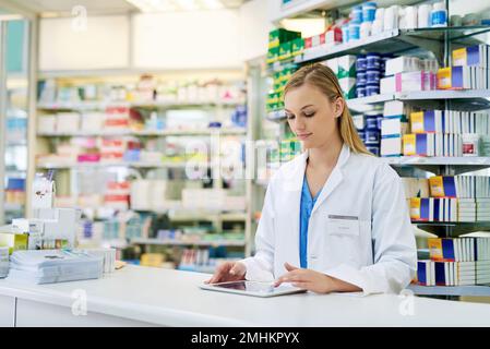 Simplifying pharmaceutical tasks with smart technology. a young pharmacist using a digital tablet at the checkout counter. Stock Photo