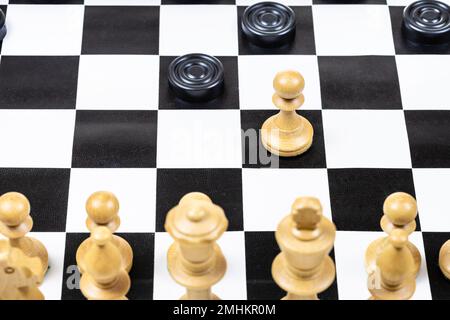 playing by different rules on the same board - black checkers and white chess figures on black white chessboard, above view of pawn and checkers piece Stock Photo