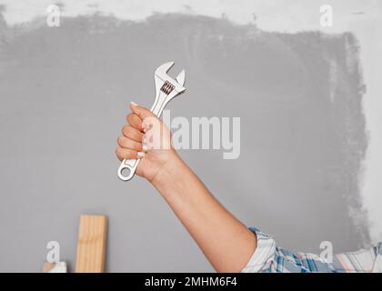 Cropped close up shot of hand holding spanner or wrench against grey wall Stock Photo