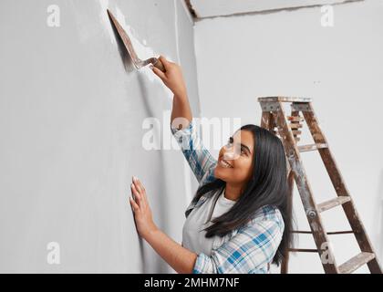 Young Indian woman plasters over cracks in wall home DIY project Stock Photo