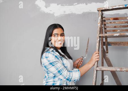 Young Indian woman plasters over cracks in wall home DIY project Stock Photo