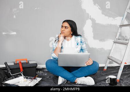 A young woman stuck for DIY ideas uses how-to guides on laptop while renovating Stock Photo