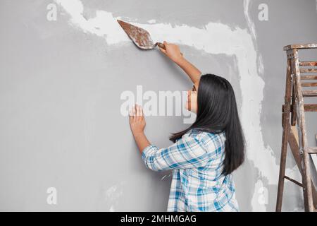 Young Indian woman plasters over cracks in wall home DIY project Stock Photo
