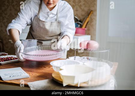 Online classes and workshops on cake decorating and baking. Female Confectioner baker make custom pink heart shape cake in kitchen Bakery. Stock Photo