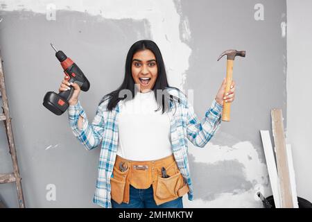 A young woman looks excited to start DIY holding hammer and screwdriver Stock Photo