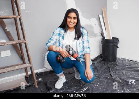 Young woman crouches on the floor holding screwdriver doing home DIY renovation Stock Photo