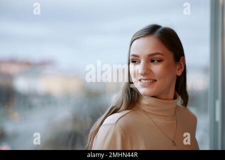 Smiling young woman looking through window Stock Photo