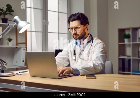 Professional male doctor filling documents using laptop computer Stock Photo