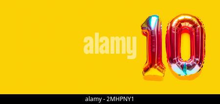 Rainbow foil balloon number, digit ten. Top view. Colored numeral on yellow background. Stock Photo