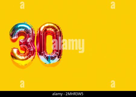 Rainbow foil balloon number, digit thirty. Top view. Colored numeral on yellow background. Stock Photo