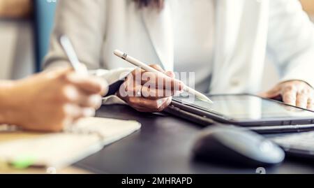 The hands of two female colleagues are using a digital tablet and a notebook. A business meeting to discuss financial management, accounting or financ Stock Photo