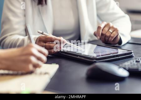 The hands of two female colleagues are using a digital tablet and a notebook. A business meeting to discuss financial management, accounting or financ Stock Photo