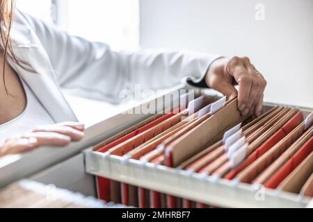 The clerk is leafing through stored folders, looking for a file or document. Concept of data storage, filing cabinet and business administration. Stock Photo