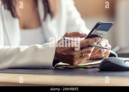 Hands of a female manager with a mobile phone, communicating with colleagues during working hours, sending messages or receiving work information. Stock Photo