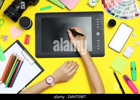 Professional designer drawing with graphic tablet at yellow table, top view Stock Photo
