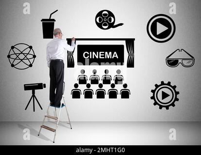 Man on a ladder drawing cinema concept on a wall Stock Photo
