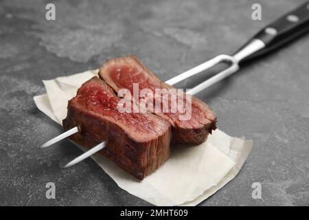 Carving fork with slices of delicious beef steak on grey table, closeup Stock Photo