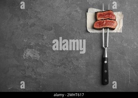 Carving fork with slices of delicious beef steak on grey table, top view. Space for text Stock Photo