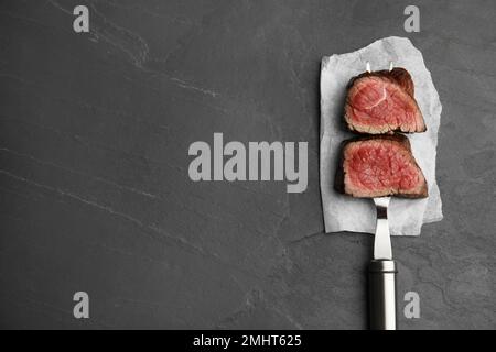 Carving fork with slices of delicious beef tenderloin on black table, top view. Space for text Stock Photo